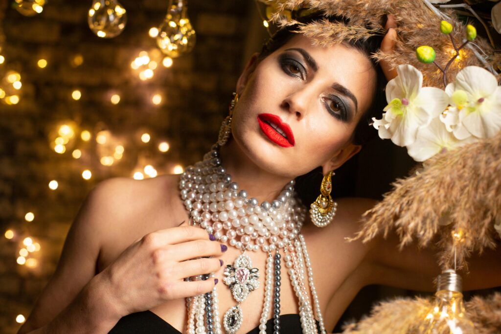 Stylish woman adorned with pearls and gold jewelry in an elegant, festive setting.
